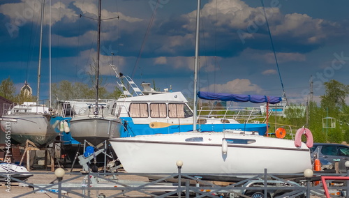 Side view of the yacht on the beds with wheels on the shore against the background of blue sky with clouds in summer