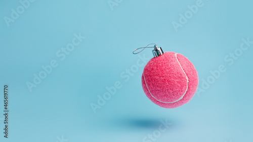 Creative Christmas layout made with flying pink tennis ball as a tree ornament vibrant red on pastel blue background. Minimal Xmas or New Year celebration concept. Minimal winter holidays idea. © Aleksandar