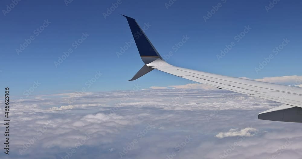 Wing of the plane with clouds over the blue sky, a view from airplane window Wing of the plane with clouds over the blue sky, a view from airplane window