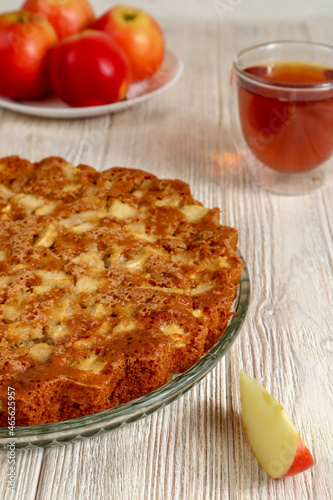 Apple pie on a plate on a wooden table against a background of red apples.