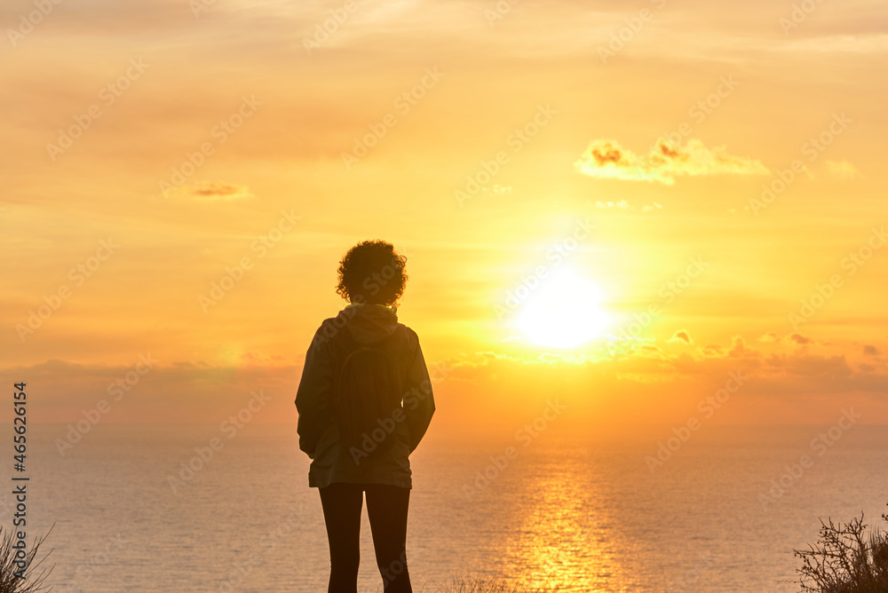 Hiker woman from behind looking at sunrise over the sea