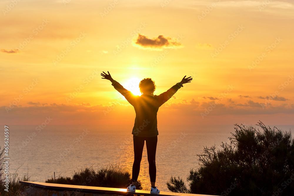 Silhouette of a female hiker with open arms as sunrise