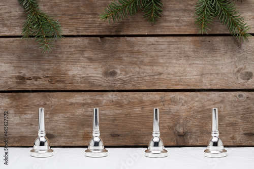 Four trombone mouthpiece representing the fourth advent on a wooden background with some small pine tree branches