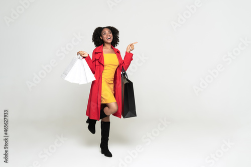 Young black woman pointing finger aside while walking with shopping bags