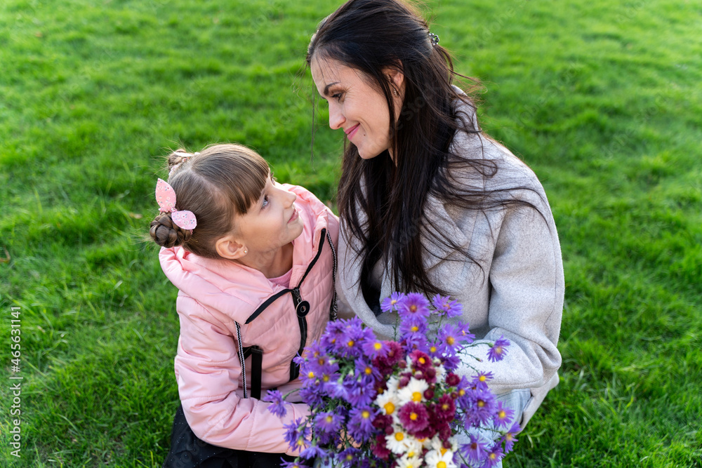 Happy mom and daughter look at each other with love. Beautiful woman with cute little girl outdoors. Flowers for mother Happy mom and daughter look at each other with love. Beautiful woman with cute little girl outdoors. Flowers for mother