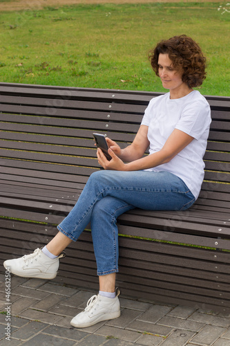 A 45-50-year-old woman is sitting on a bench with a mobile phone in her hands