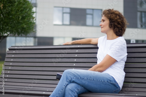 A 45-50 years old woman is sitting on a bench and resting.