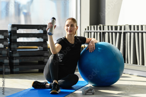 Woman with the Exercise Ball is engaged in the gym, holding shaker, water bottle. Middle-aged Fitness Woman. Sport and healthy lifestyle concepts