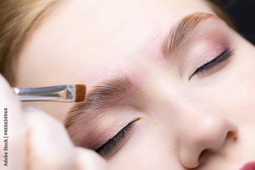 close-up of the eyebrows, on which the master evenly applies and distributes laminating compounds, thereby directing their growth