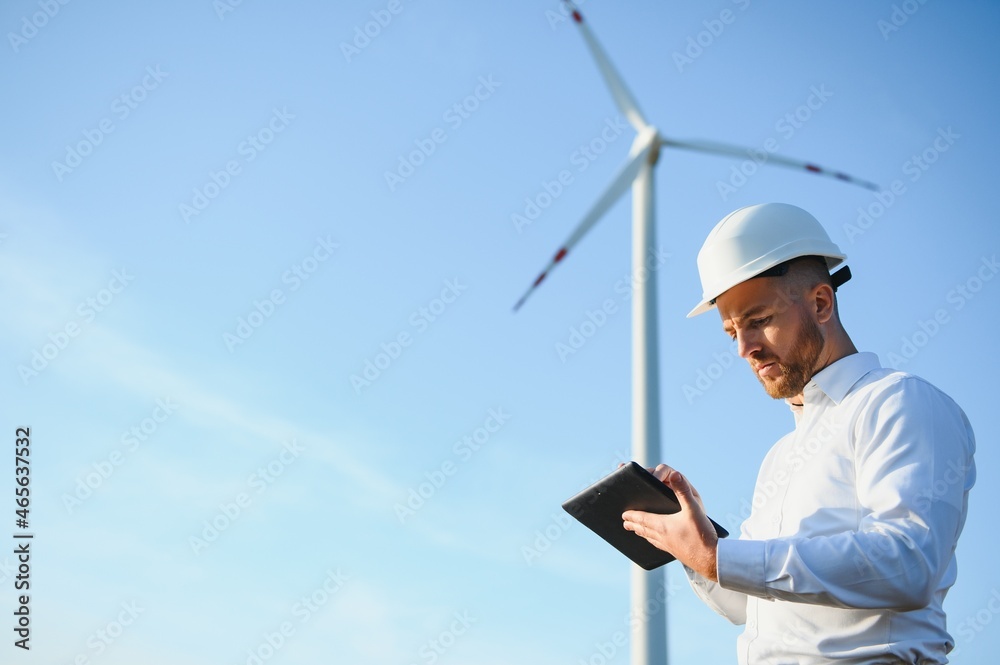 Engineer is checking energy production on wind turbine. Worker in windmills park in helmet. Engineer is checking energy production on wind turbine. Worker in windmills park in helmet.