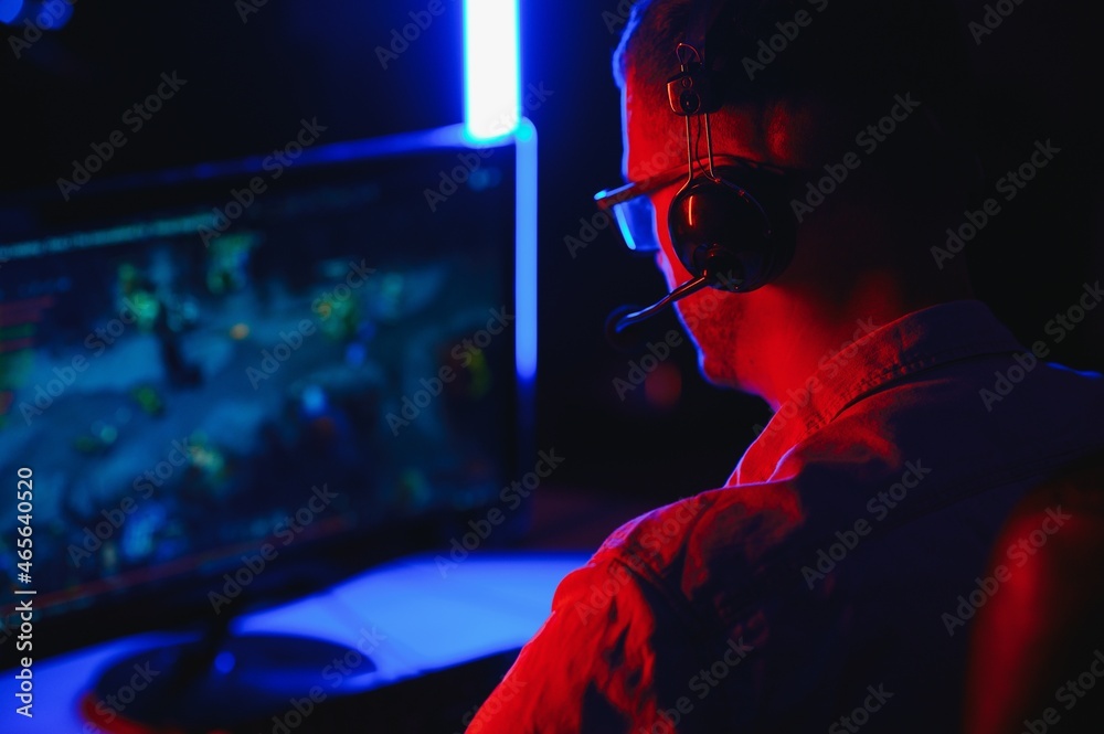 Professional Gamer Plays Video Game on His Computer. He's Participating in Online Cyber Games Tournament or in Internet Cafe. He Wears Glasses and Talks into Microphone. Professional Gamer Plays Video Game on His Computer. He's Participating in Online Cyber Games Tournament or in Internet Cafe. He Wears Glasses and Talks into Microphone.