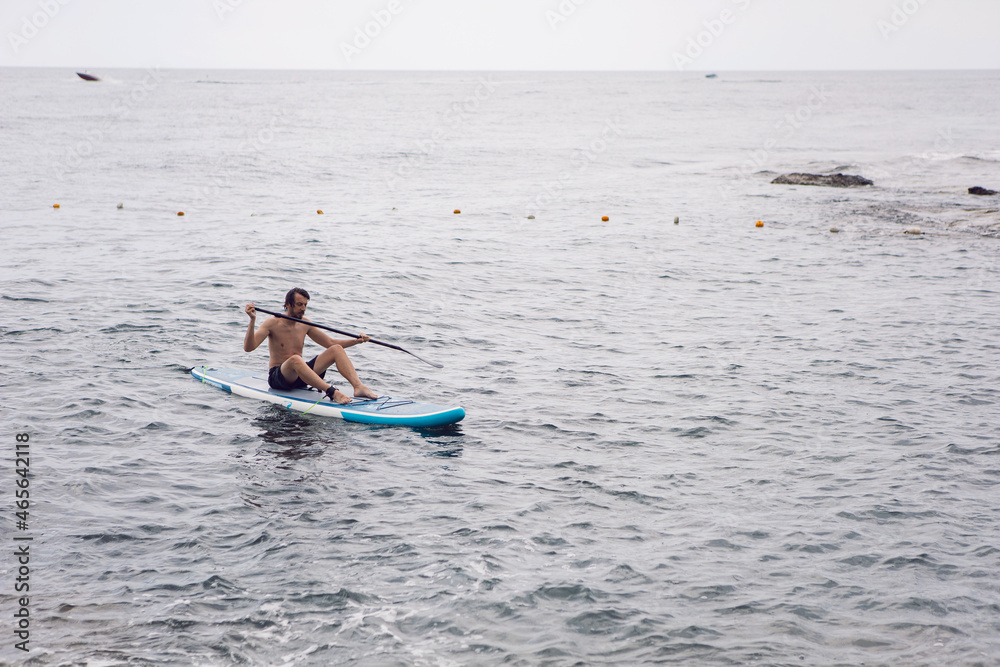 man with a beard swims on stand up paddle board on quiet blue ocean. Sup surfing in water