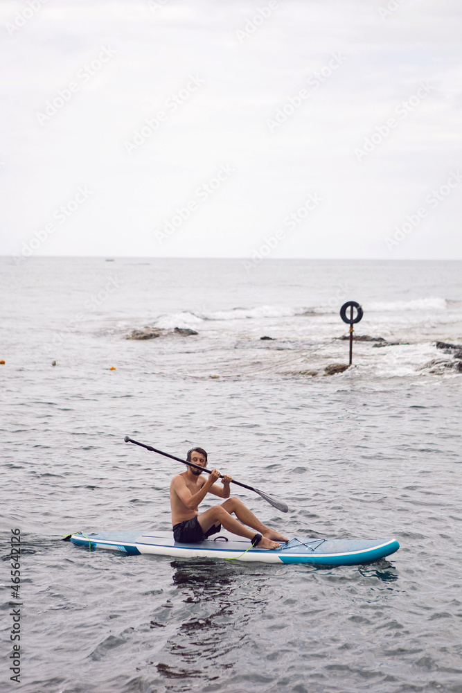 man with a beard swims on stand up paddle board on quiet blue ocean. Sup surfing in water