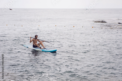 Obraz na płótnie man with a beard swims on stand up paddle board on quiet blue ocean. Sup surfing in water w salonie
