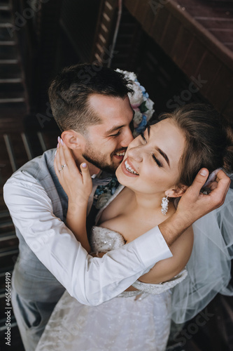 Close-up wedding portrait of beautiful, cheerful and happy newlyweds. Stylish smiling bearded groom in a gray waistcoat hugs a young bride.