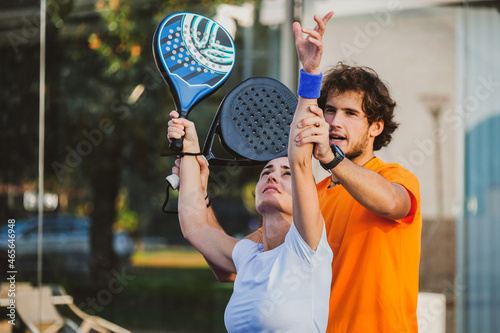 Young teacher is monitoring teaching padel lesson to his student - Coach teaches girl how to play padel on the outdoor tennis court