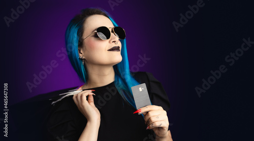 Large banner Woman in black friday, shopping, expressions with sunglasses, shopping bag and credit card in hand, blue hair, copy space, black background, neon style for websites, billboards and boards © Tim Paza May
