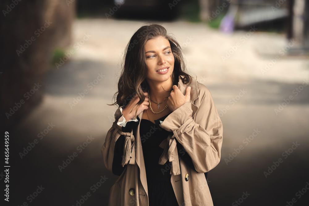 Autumn portrait of a young pretty girl in a coat. A girl in a trendy trench coat walks in the old town