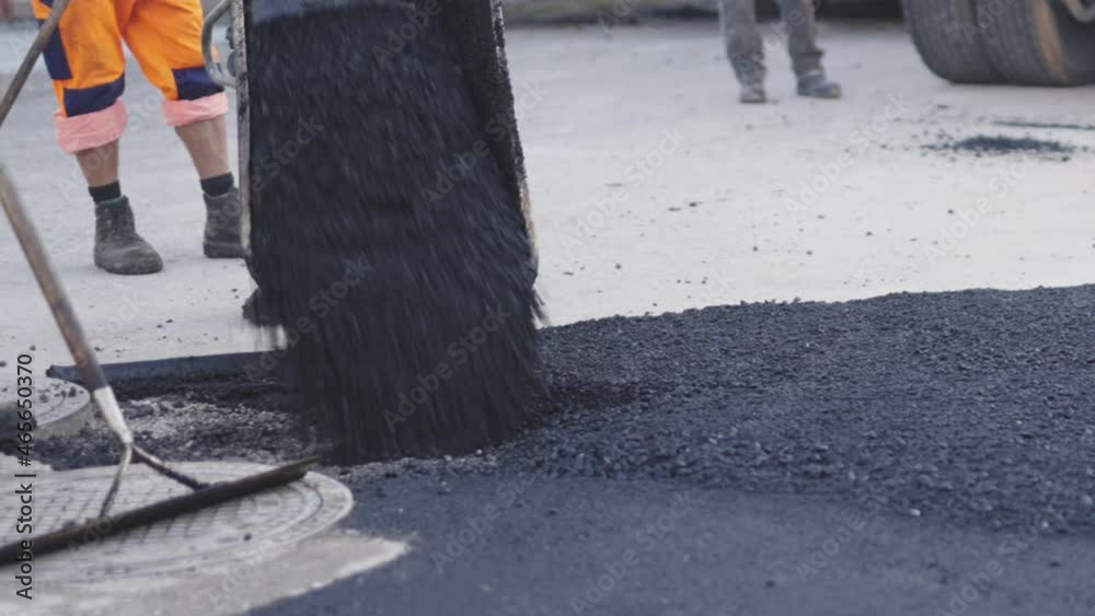 Heißer Asphalt wird mit den Schubkarren und der Asphaltiermaschine an die richtige Stelle gekippt.