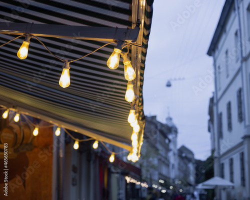 Evening restaurant terrace lamps light. European old city street exterior. Cold weather cloudy day