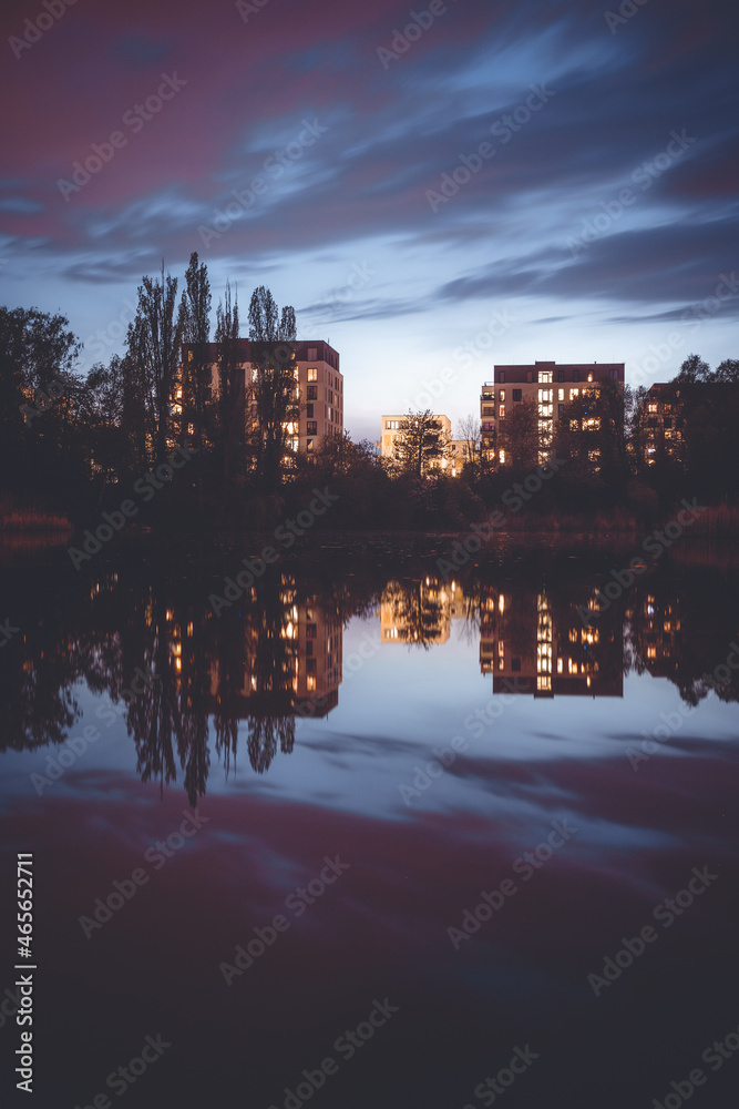 Buildings at a lake with purple clouds in the sky. Reflection of the buildings and sky visible.