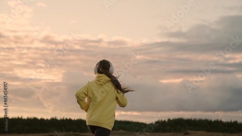 Free young woman runs in summer in park at dawn listens to music with headphones. Training jogging. Healthy jogging and outdoor exercise concept. Listen to music without the Internet and play sports
