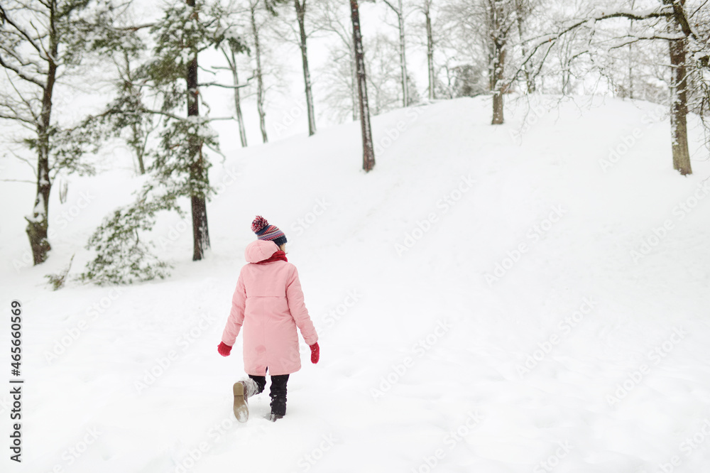 Adorable girl having fun in beautiful winter park during snowfall. Cute child playing in a snow. Winter activities for family with kids.