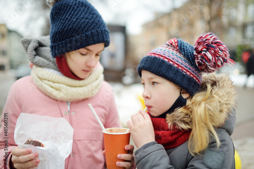 Two young sisters having hot chocolate and snacks on chilly winter day at city park.