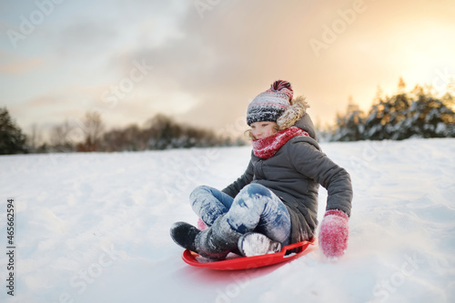 Funny little girl having fun with a sleigh in beautiful winter park. Cute child playing in a snow.