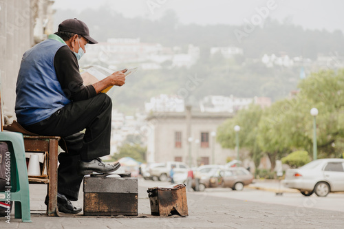 Man working as a shoe polisher in city park - older man reading newspaper while working - workers in latin america photo
