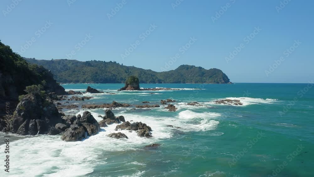 Aerial: Rocky coastline with waves crashing over rocks. Golden sandy beach. Sailors Grave, Coromandel Peninsula, New Zealand Aerial: Rocky coastline with waves crashing over rocks. Golden sandy beach. Sailors Grave, Coromandel Peninsula, New Zealand