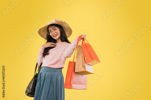 Beautiful woman in hat and glasses smiling with hand carrying shopping paper bag