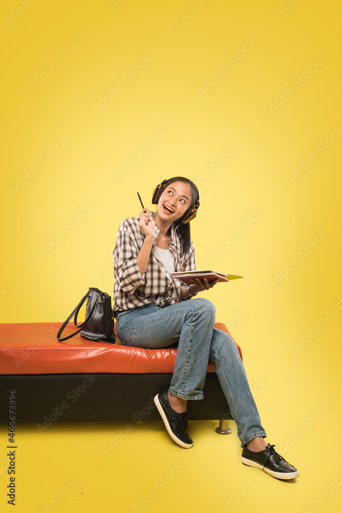 beautiful smiling girl wearing headphones holding pen and book while looking up with copyspace