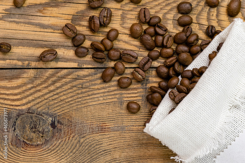 Coffee beans are scattered from a canvas bag on a wooden background. Space for text on a canvas bag, coffee grains on a wooden background.