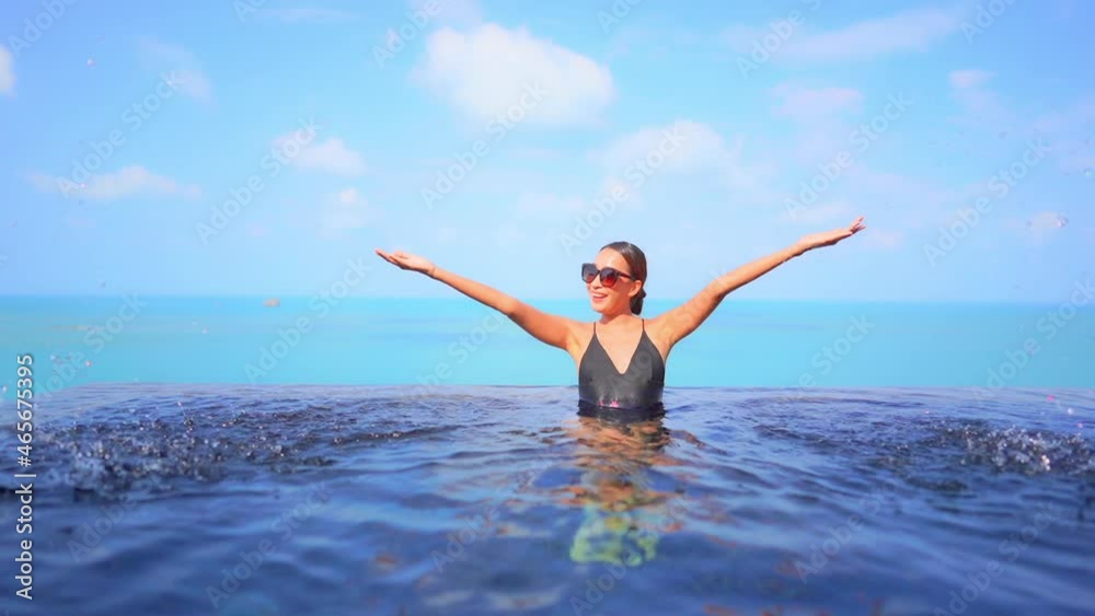 With the ocean as a backdrop, a pretty young woman playfully splashes water in the swimming pool. With the ocean as a backdrop, a pretty young woman playfully splashes water in the swimming pool.