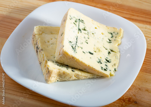 Two slices of piquant soft blue cheese served on white plate on wooden surface