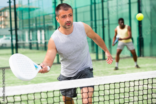 Portrait of man playing with male partner padel doubles game on outdoors court © JackF