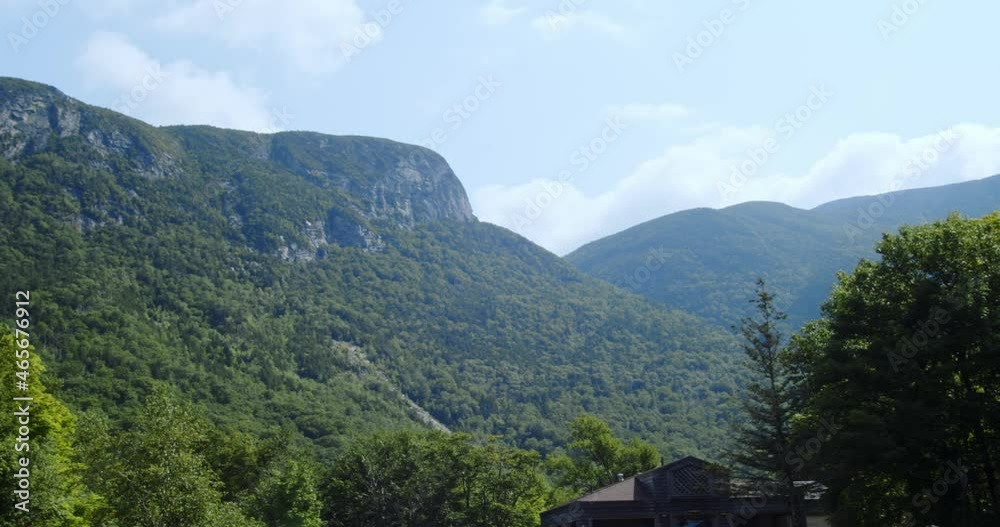 Granite mountains covered in vegetation tower over treetops as the camera pans from a low angle against a blue sky. Granite mountains covered in vegetation tower over treetops as the camera pans from a low angle against a blue sky.