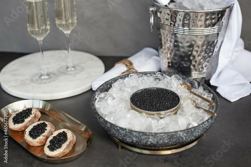 Black caviar in can on ice, caviar sandwich on golden plate, champagne in glass