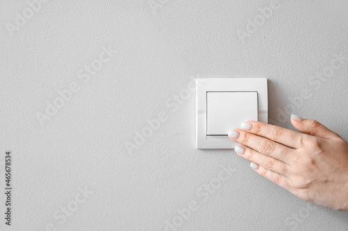 Woman switching off light on light wall, closeup photo