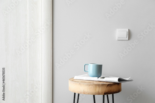 Table with cup and newspaper near light wall © Pixel-Shot