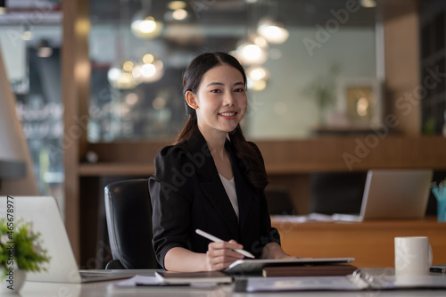 Portrait of young smiling cheerful entrepreneur in modern office working with digital tablet for financial analysis