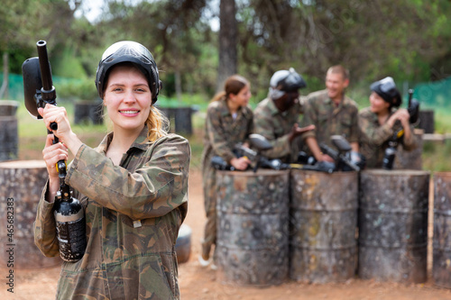 Happy woman and her paintball sport team in protective uniform at shooting range