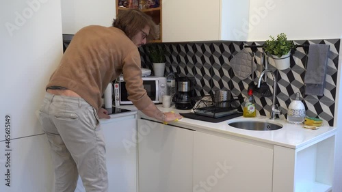 A man maid is cleaning the house kitchen with a yellow clothe and suddently leaves photo
