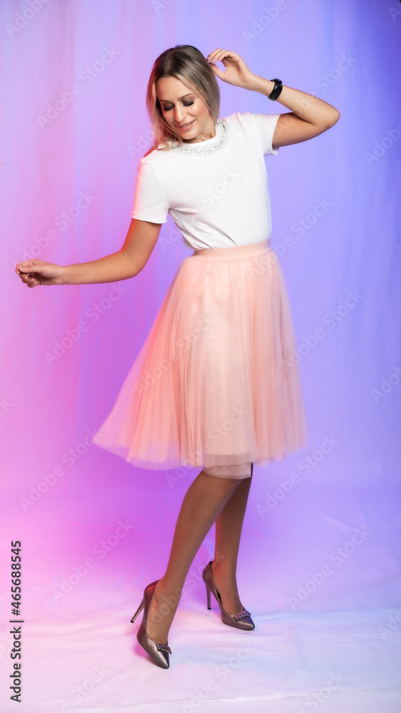 beautiful woman portrait in studio posing. A girl in a white blouse, a T-shirt and a pink, peach pleated skirt laughs, spins, dances. colored, crimson purple background. holiday, new year, birthday beautiful woman portrait in studio posing. A girl in a white blouse, a T-shirt and a pink, peach pleated skirt laughs, spins, dances. colored, crimson purple background. holiday, new year, birthday