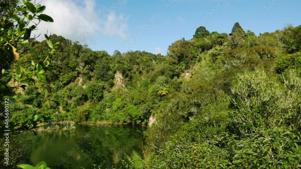 Panning shot of natural lake surrounded by green trees growing on hill in Waimangu during summer Panning shot of natural lake surrounded by green trees growing on hill in Waimangu during summer