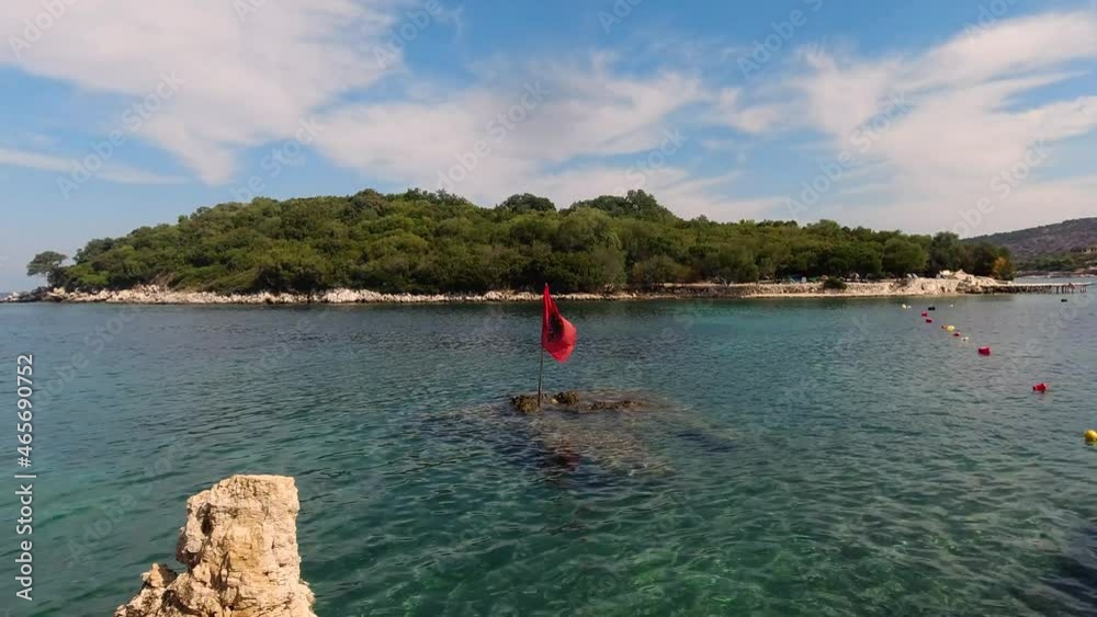 Stunning scenery of Albanian Flag waving in front of Ksamil Island on clear day Stunning scenery of Albanian Flag waving in front of Ksamil Island on clear day