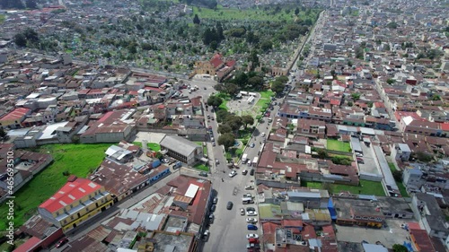 Drone aerial footage of urban colonial city park Parque El Calvario in Central American highlands city Quetzaltenango, Xela, Guatemala with traffic driving around on a sunny day. Camera tracking back. photo