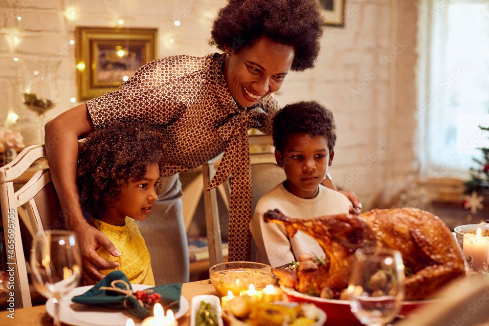 Happy African American mother with kids enjoys in Thanksgiving lunch at dining table.