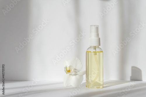 Mock-up of glass bottle with spray bottle and orchid flower in sunlight  casting shadow on white background. Skin care concept  spa treatments  natural cosmetics